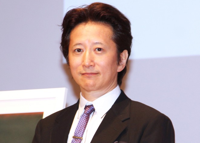 Manga artist Hirohiko Araki at a 2023 press event—his signature poised mid-sketch; rich indigo jacket echoes JoJo color motifs.